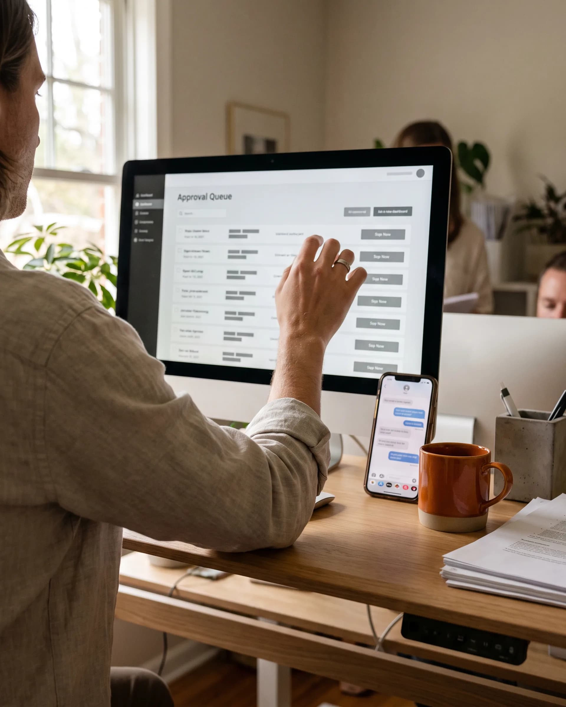 A person at a standing desk reviewing an approval queue on a monitor
